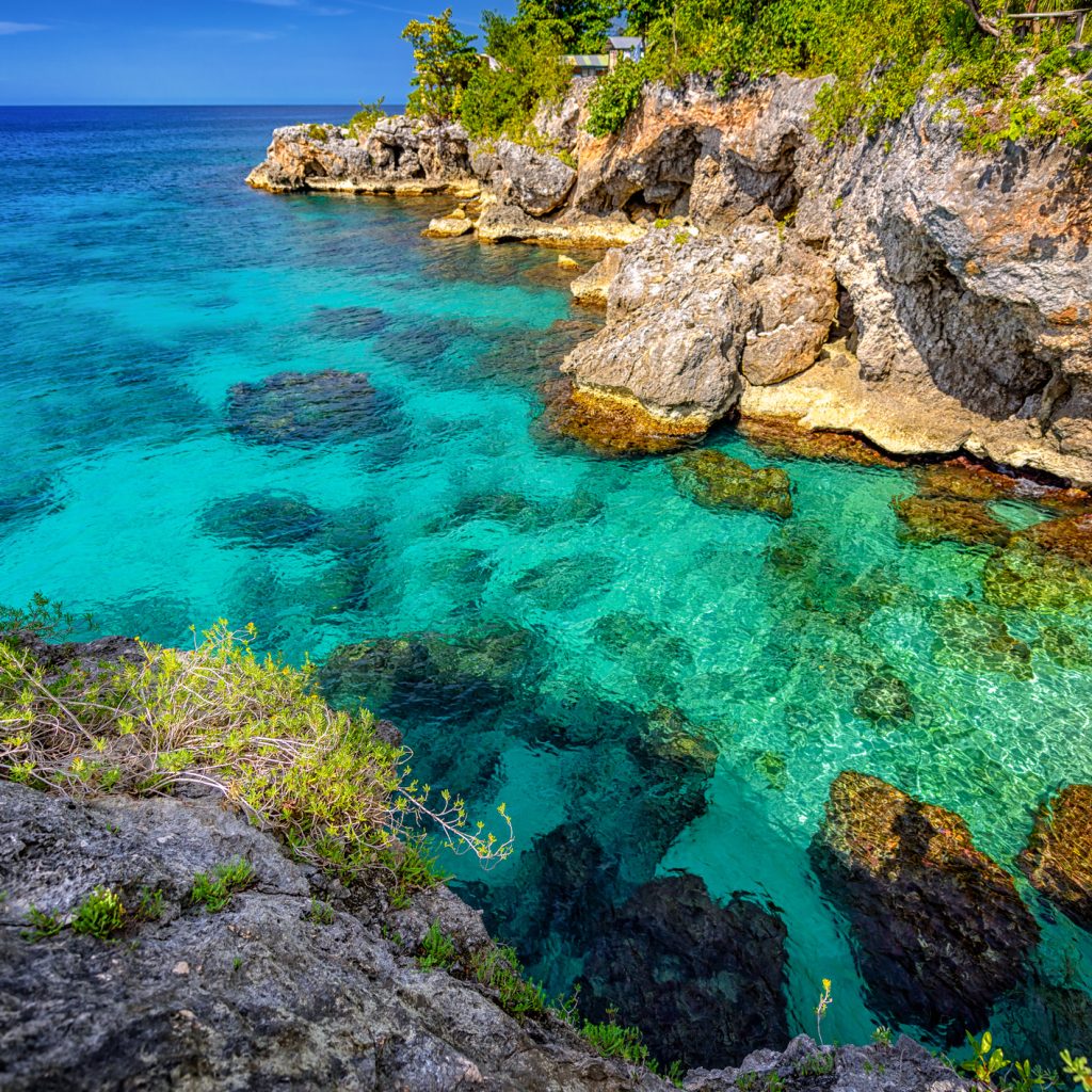 Beautiful clear turquoise water near rocks and cliffs in Negril Jamaica. Caribbean paradise island and water at the seaside with a blue sky and nice day light